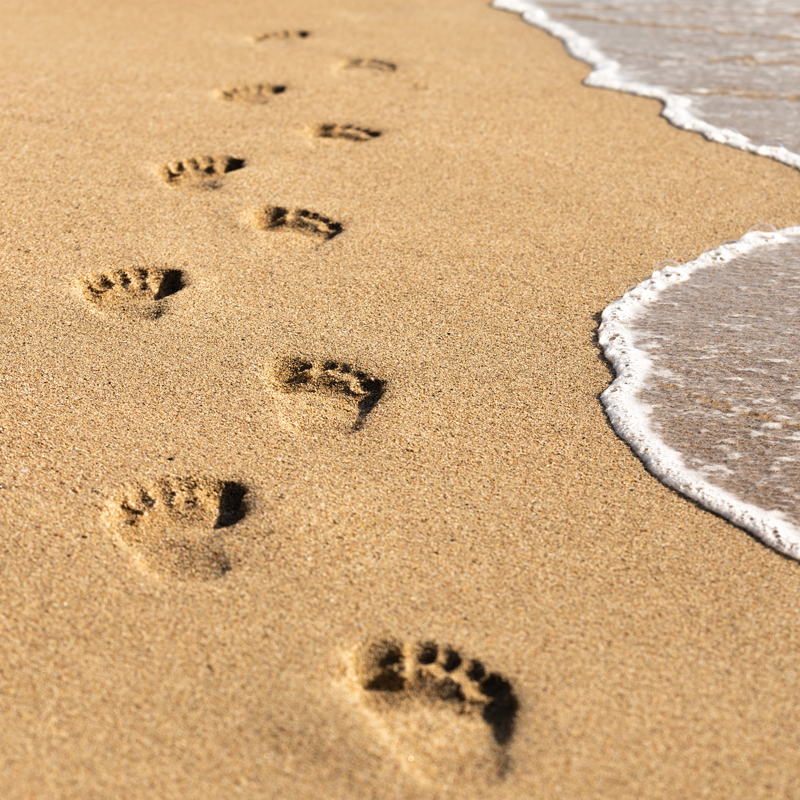 Fußspuren im Sand am Strand neben einer anrollenden Welle