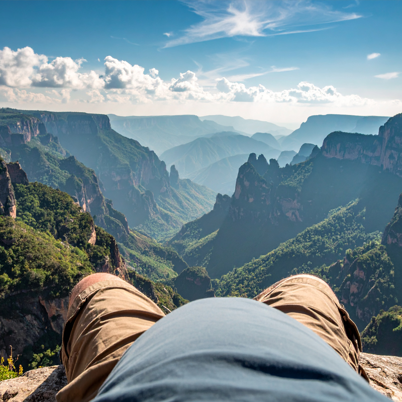 Blick von einer Person auf Berge mit bewaldeten Tälern unter blauem Himmel mit Wolken