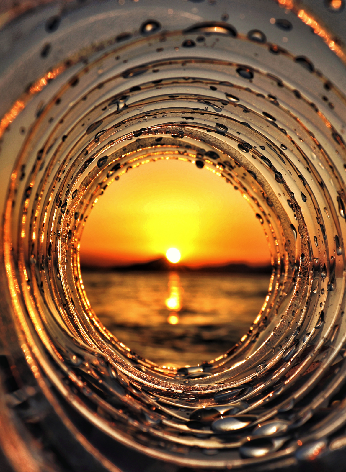 Sonnenuntergang über dem Meer durch eine spiralförmige transparente Röhre mit Wassertropfen